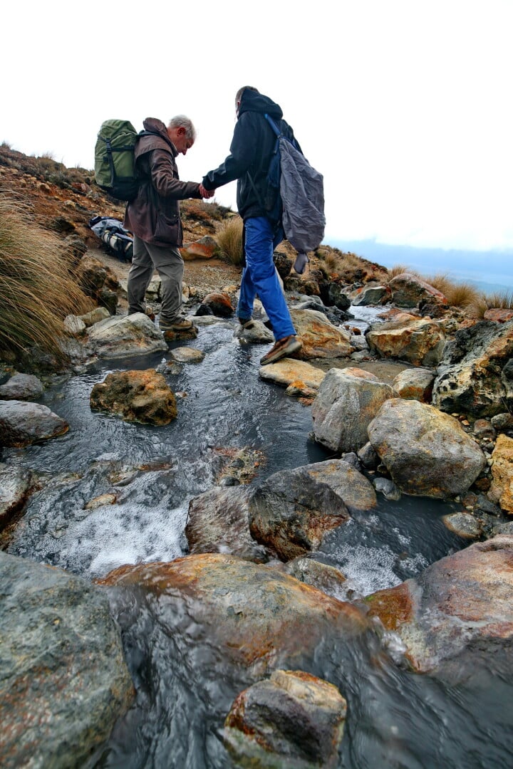 One gentleman helps another cross the tepid Ketetahi stream, Tongariro Alpine Crossing
